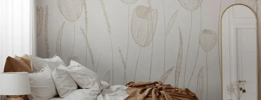 A modern bedroom with a bed made up with white bed linen and a beige blanket. The wall is adorned with a subtle wall mural featuring a minimalist linear pattern of tulips in shades of beige and gold.