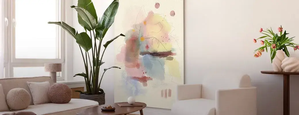 A large XXL painting with an abstract motif in the living room between an armchair and a sofa A modern living room with elements of classic elegance. A large abstract painting hangs on the wall, characterised by pastel splashes of colour in shades of pink, blue, yellow and beige, complemented by delicate, linear accents.